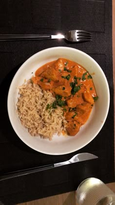 a white plate topped with rice and meat next to a fork, knife and spoon