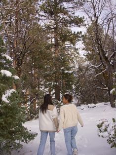 two women walking in the snow holding hands and looking at each other's back