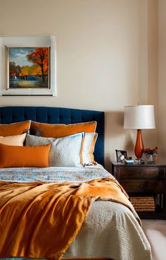 a bed with orange and white pillows in a bedroom next to a painting on the wall