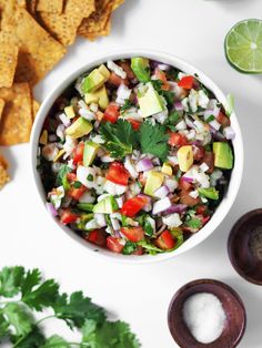 a white bowl filled with salsa surrounded by tortilla chips and cilantro