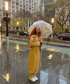 a woman standing in the rain holding an umbrella and looking off into the distance with buildings in the background