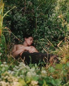 a shirtless man laying in the grass with his head under some trees and bushes