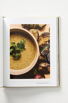 an open book with food on it and a bowl of soup in the middle, surrounded by grilled vegetables