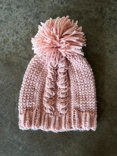 a pink knitted hat with a pom - pom on top