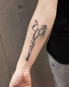 a person with a tattoo on their arm holding a pair of scissors in one hand