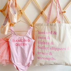 three ballet leotards hanging on the wall next to a canvas bag that says dancing queen