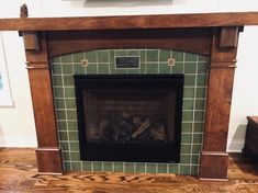 a fireplace in a living room with green tile and wood trimming on the mantle