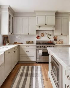 a kitchen with white cabinets and an oven in the center, along with a striped rug on the floor