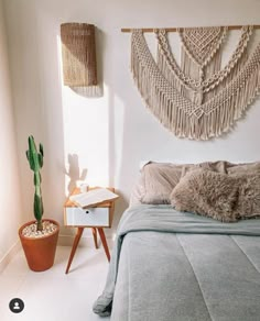 a bedroom with a bed, plant and macrame wall hanging