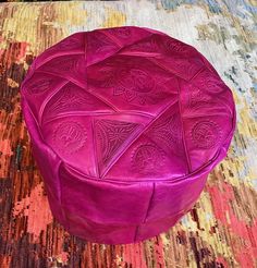 a purple ottoman sitting on top of a colorful rug next to a wooden table with an intricate design