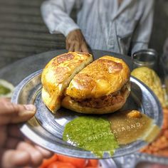 a person holding a plate with a sandwich on it and some vegetables in the background