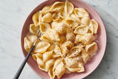 a pink bowl filled with pasta on top of a marble countertop next to a fork