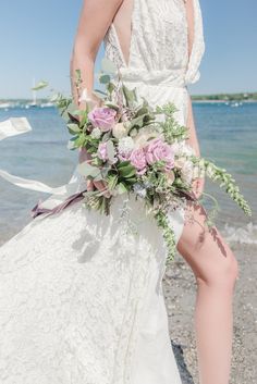 a woman in a wedding dress holding a bouquet on the beach with her legs crossed