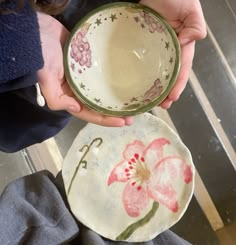 a person holding two plates with flowers on them and one has a flower painted on it