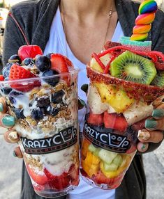 a woman holding two cups filled with fruit and yogurt ice cream sundaes