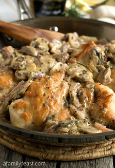 a pan filled with chicken and mushrooms on top of a wooden table next to bread