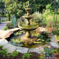 a water fountain in the middle of a garden with lily pads and plants around it