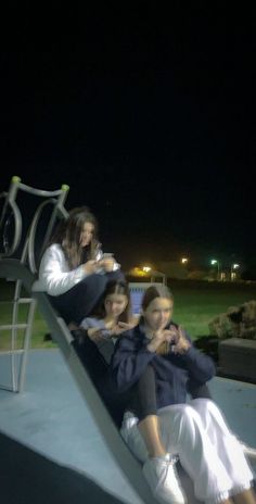 three women sitting on a slide at night