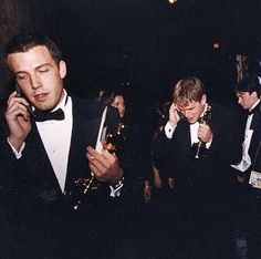 two men in tuxedos are talking on their cell phones at an oscars event