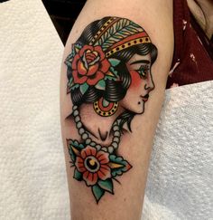 a woman's head with flowers and leaves on her arm, done by tattoo artist