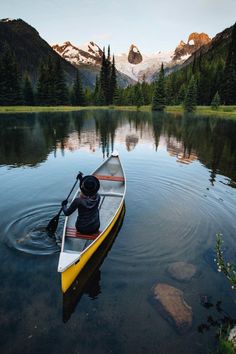 a person in a canoe paddling on the water with mountains in the background at sunset