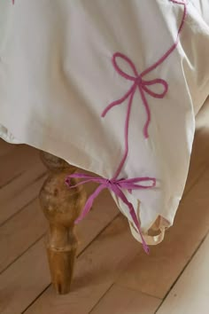 a white pillow with pink ribbon tied to it on a wooden floor under a bed