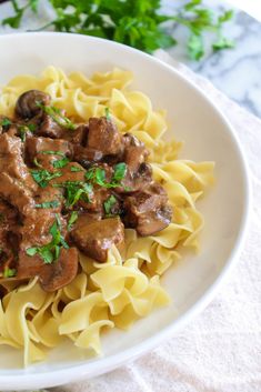 a white bowl filled with pasta and meat covered in sauce, garnished with parsley