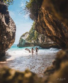 two people are walking into the water near some rocks