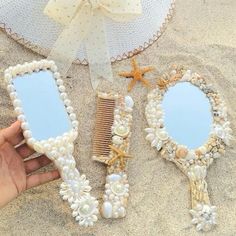 someone is holding three mirrors in the sand with seashells and starfish on them