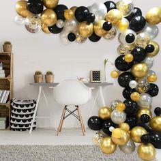 black, white and gold balloons are hanging from the ceiling in an office space with a chair