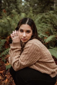 a woman kneeling down in the woods with her hands on her face and looking at the camera