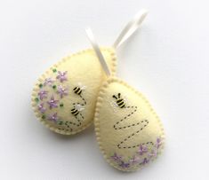 two small felt mittens with flowers and bees hanging from the strings on a white background