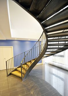 a spiral staircase in an empty building with blue walls and tile flooring on either side