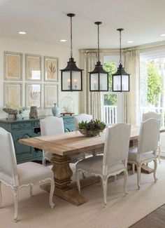 a dining room table with white chairs and hanging lights