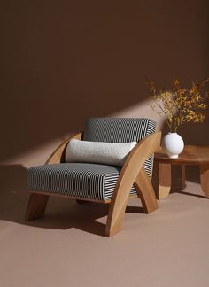 a chair and table with a vase sitting on top of it in front of a brown wall