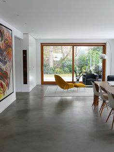 a dining room table and chairs in front of a large window with an abstract painting on the wall