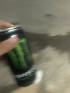 a hand holding a can of monster energy drink in it's left hand,