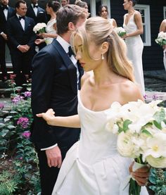 a bride and groom standing in front of a group of people wearing tuxedos