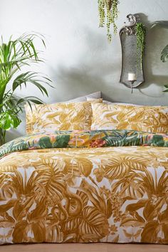 a bed covered in a yellow and green comforter next to a potted plant