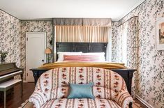 a bed sitting next to a piano in a room with floral wall paper on the walls