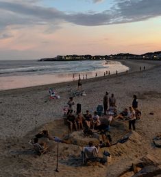 people are sitting on the beach at sunset