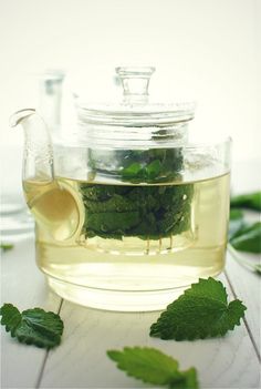 a glass teapot filled with green leaves and liquid on top of a wooden table