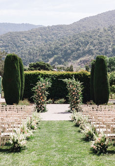 an outdoor ceremony setup with rows of chairs and flowers on the aisle, surrounded by greenery