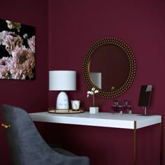 a desk with a mirror, lamp and vase on it in front of a purple wall