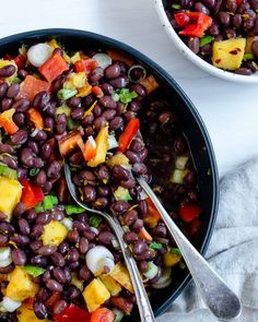 two bowls filled with black beans and veggies on top of a white table