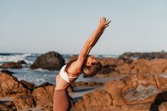 a woman doing yoga on rocks near the ocean