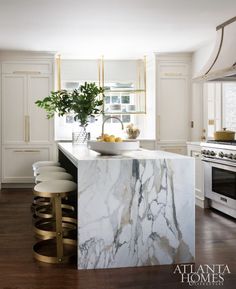 a kitchen with marble counter tops and gold accents on the island, along with stools