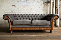 an old leather couch sitting on top of a wooden floor next to a brick wall