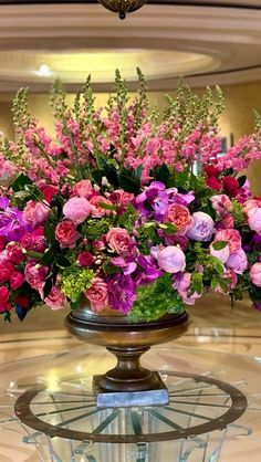 a vase filled with pink and purple flowers on top of a glass display case in a building