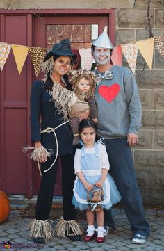 a family dressed up for halloween standing in front of a building with pumpkins and decorations